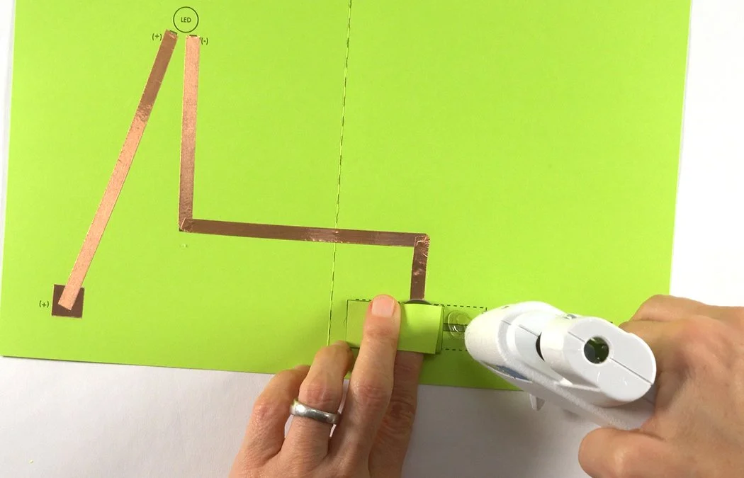 Hold the battery tightly in the pocket. Lift up 1 tab and place hot glue underneath.
