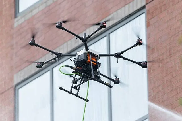 A drone equipped with six propellers flying outdoors near a building.