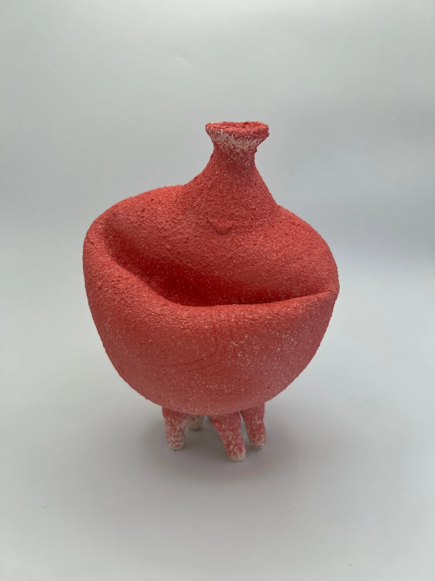A small figurine of a pig made of pink material with a rough texture, standing on four legs, with a rounded body, a snout, and small ears.