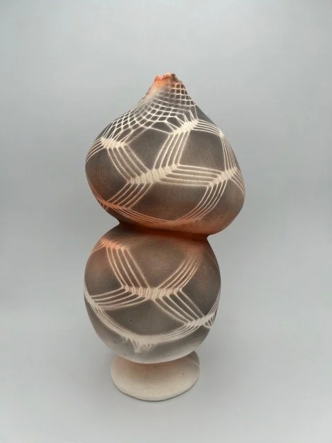 Decorative ceramic vase with geometric stripe patterns, set against a plain background, reflected on a glossy surface.
