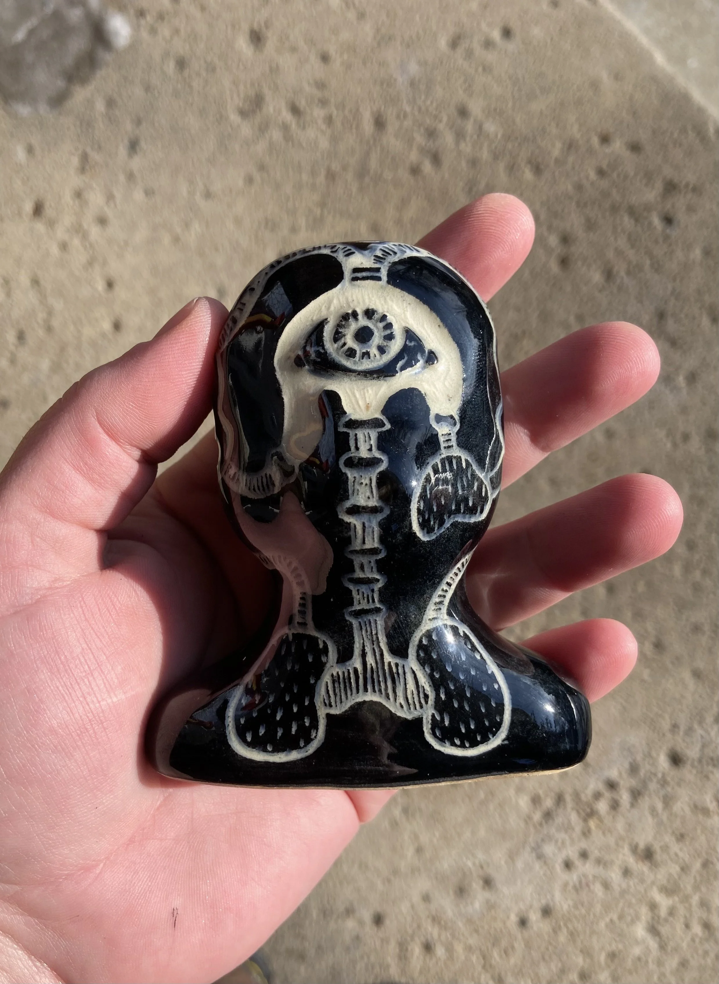A hand holding a small black and white skull-shaped object with intricate designs, against a sandy background.