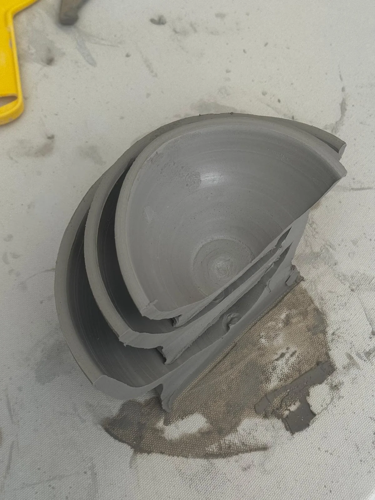 A partially broken cylindrical gray duct or pipe with a circular cross-section, placed on a textured surface with debris and dust around it.