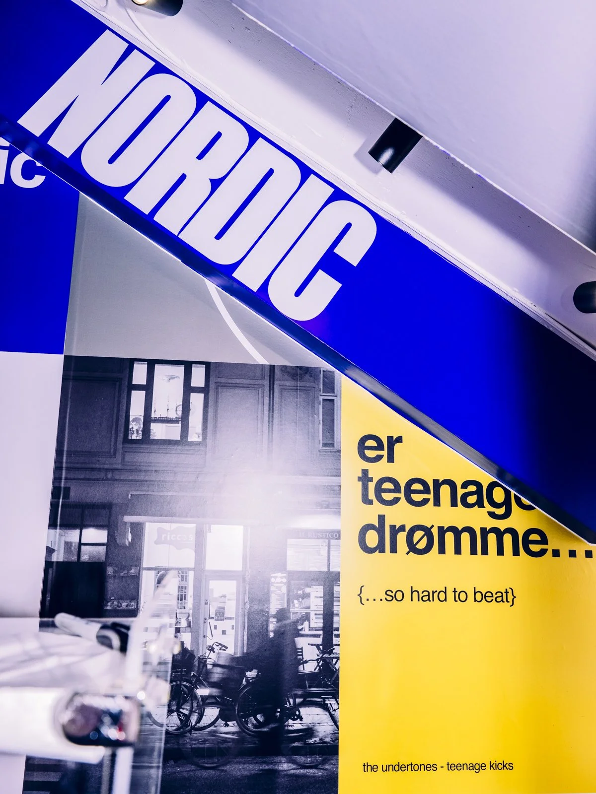 Partial view of a magazine page with colorful text and images, including a large headline 'NORBIC' in white on a blue background, and a yellow section with black text saying 'er teenage drømme... {...so hard to beat}', along with a black and white ph