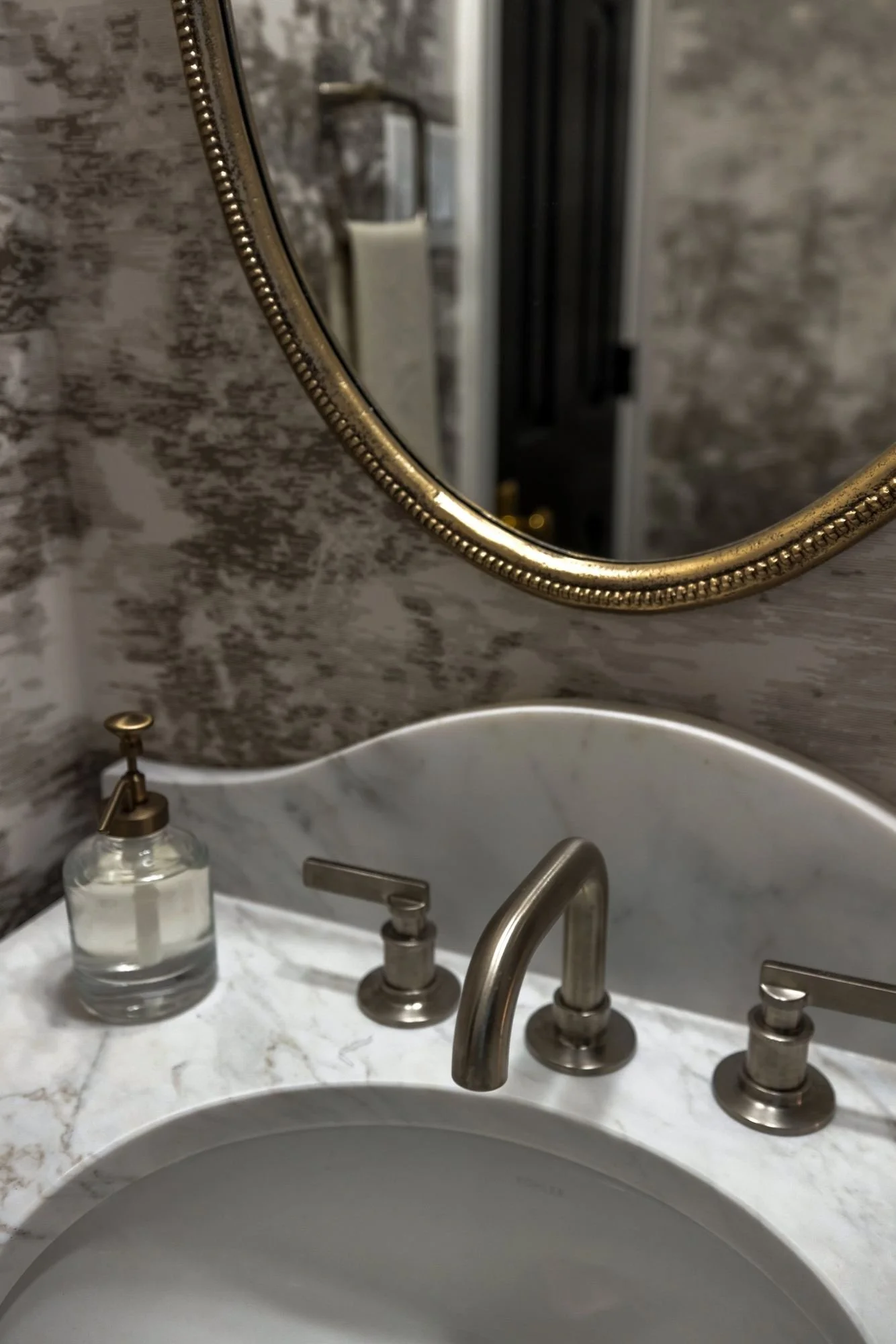 Detail of a brass faucet and marble sink against mural wallpaper
