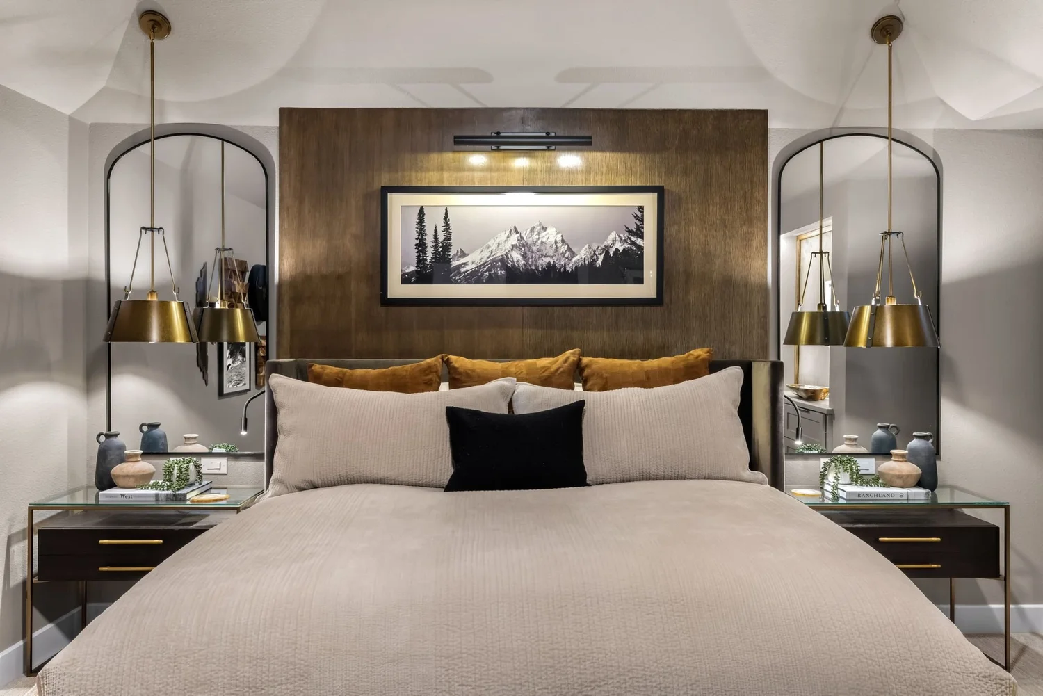 Primary bedroom with wood feature wall, mountain art and brass pendants