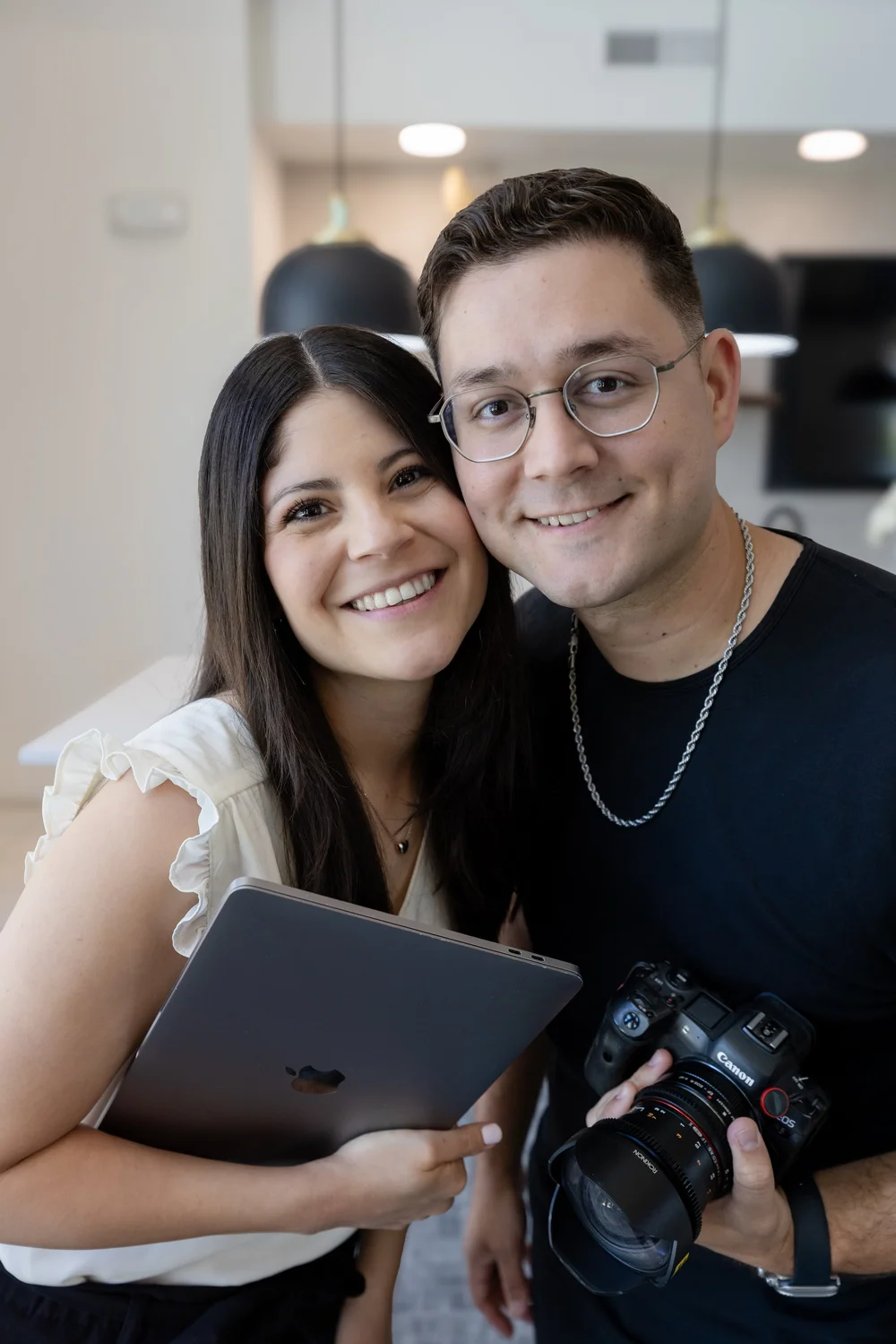 Will and Andrea Stahl smiling together, holding a laptop and a camera