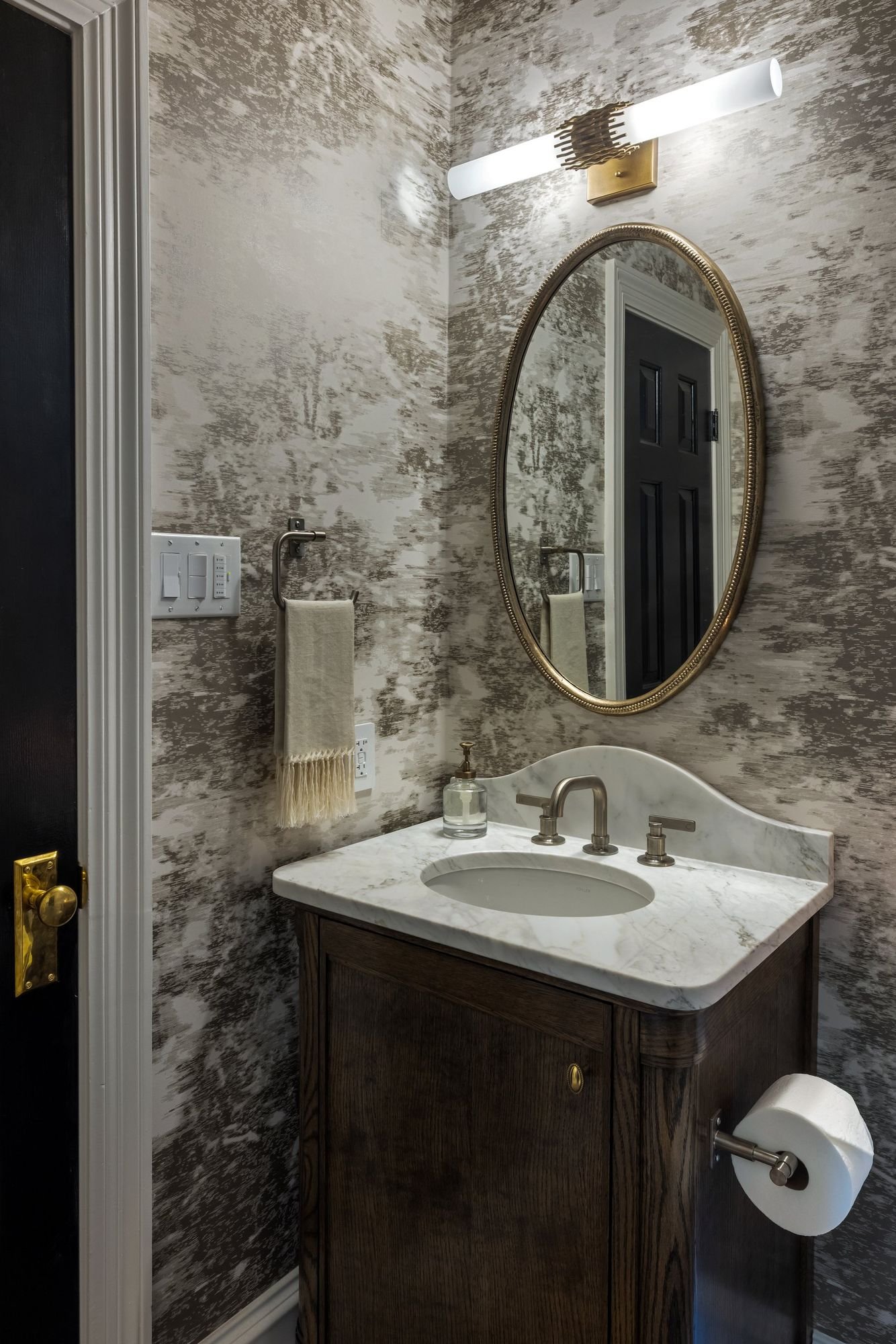 Powder room with mural wallpaper, oval brass mirror and dark wood vanity