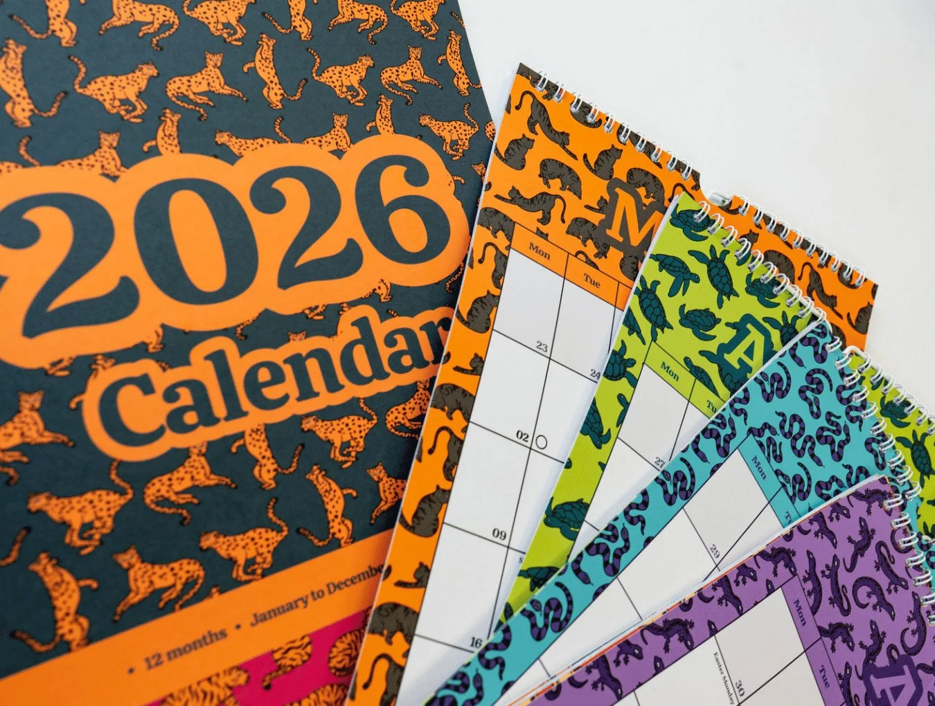 A 2026 calendar with a tiger print cover and multiple spiral-bound monthly pages, each featuring colorful animal patterns, illustrated and designed by Sprout Design.