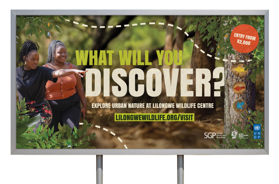 Billboard advertising Lilongwe Wildlife Centre, featuring two women pointing towards trees and colorful signs, with text about discovering wildlife, entry costs, and a website link.