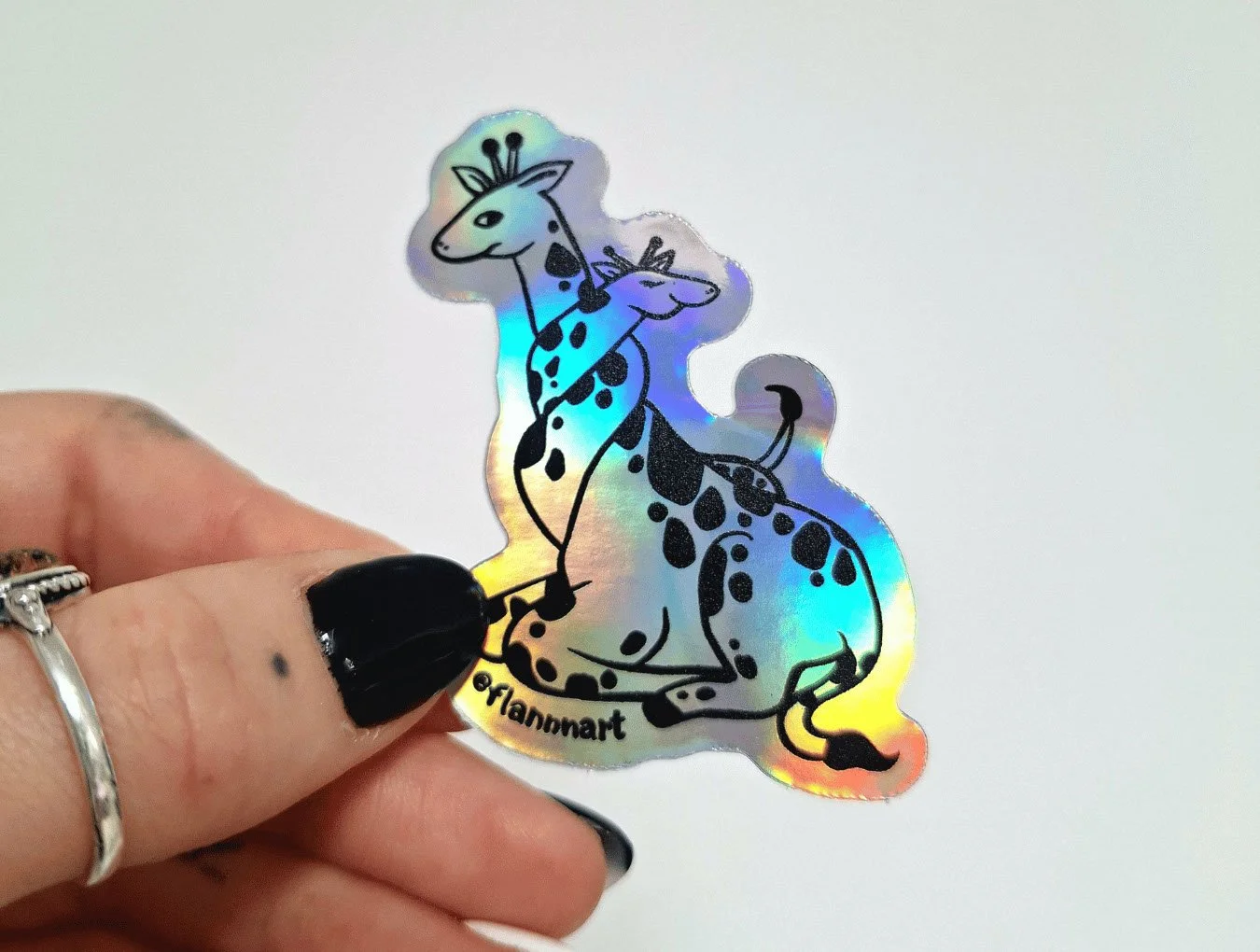 Holographic sticker of two cartoon giraffes with black spots, sitting with a playful expression. The sticker was designed by Sprout Design.