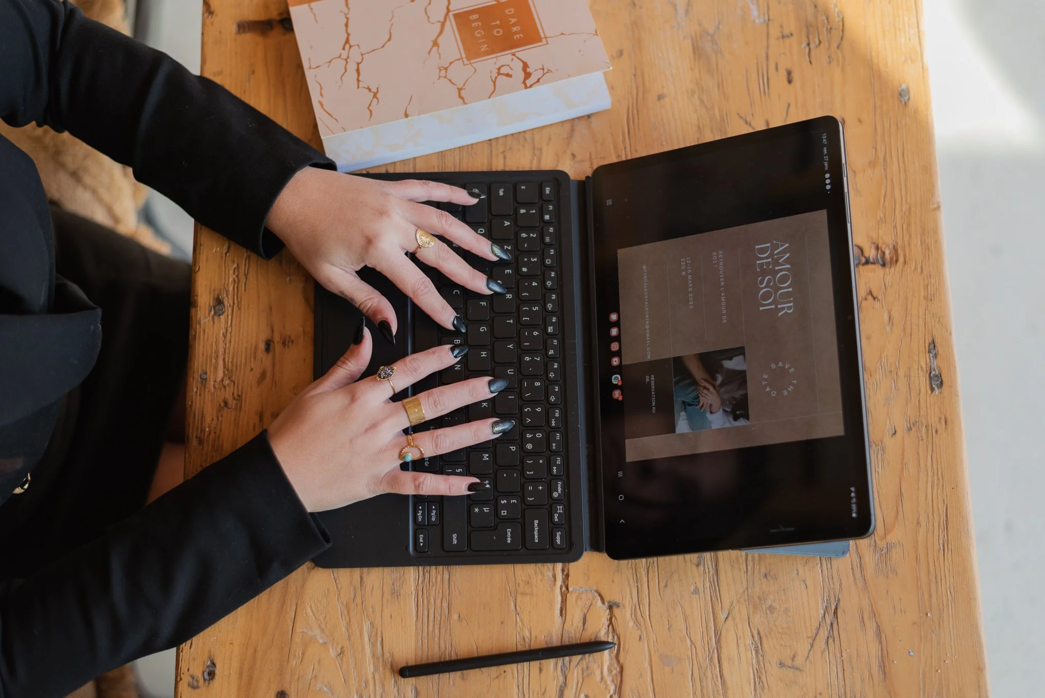 Person using a small keyboard attached to a tablet on a wooden table, with a book nearby.