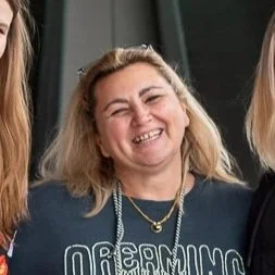 A woman with blonde hair smiling and wearing a dark sweatshirt with the word 'Dreaming' visible.