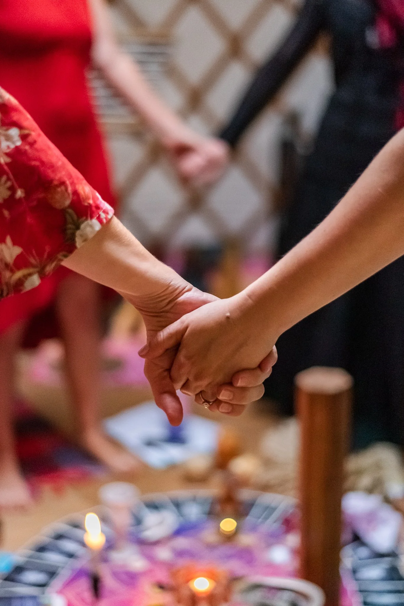 Two people holding hands during a ceremony, with blurred background showing others and a colorful altar.