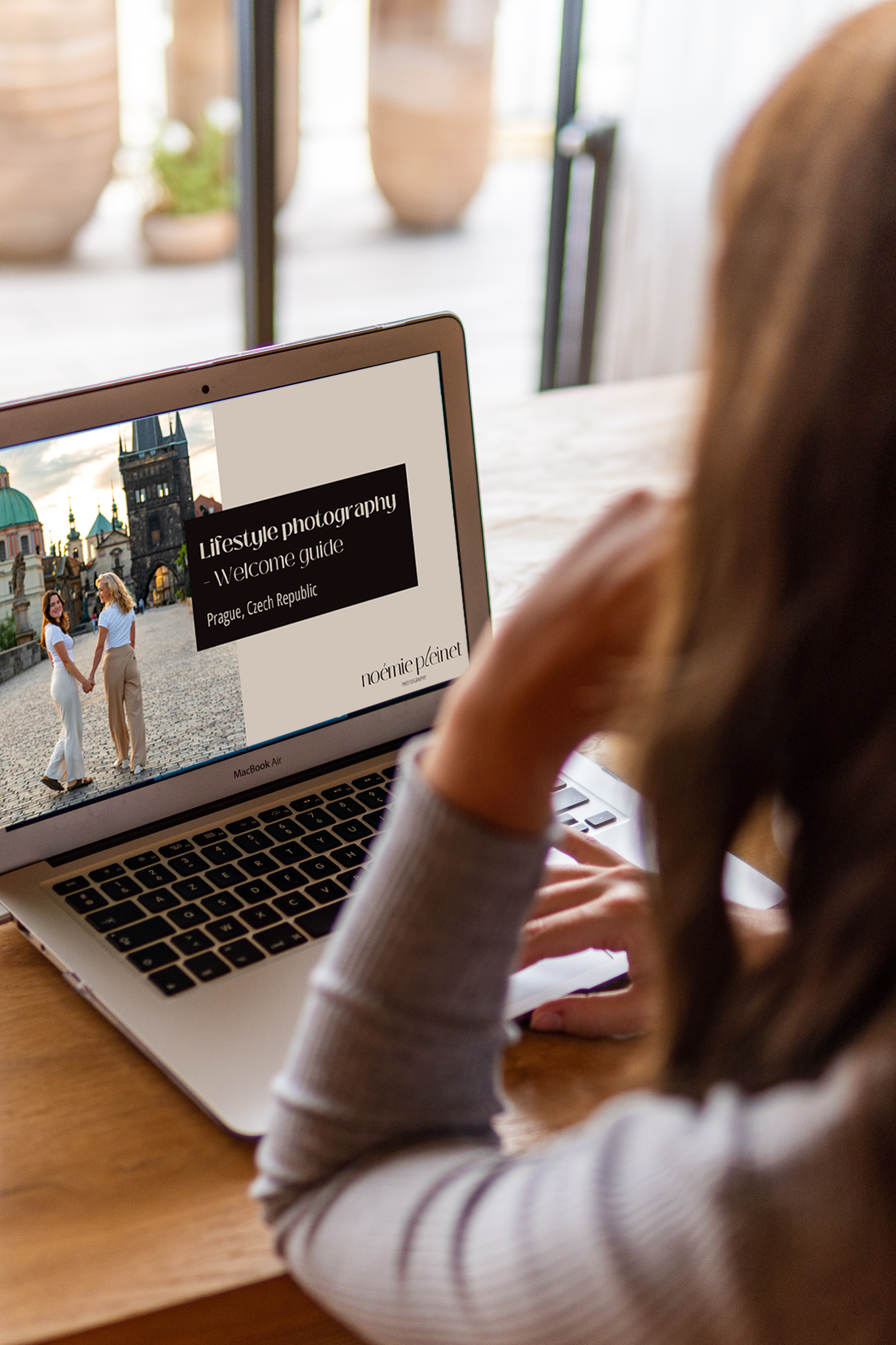 A person viewing a laptop screen displaying a travel photography guide for Prague, Czech Republic, with an image of two women holding hands in a historic Prague city square.