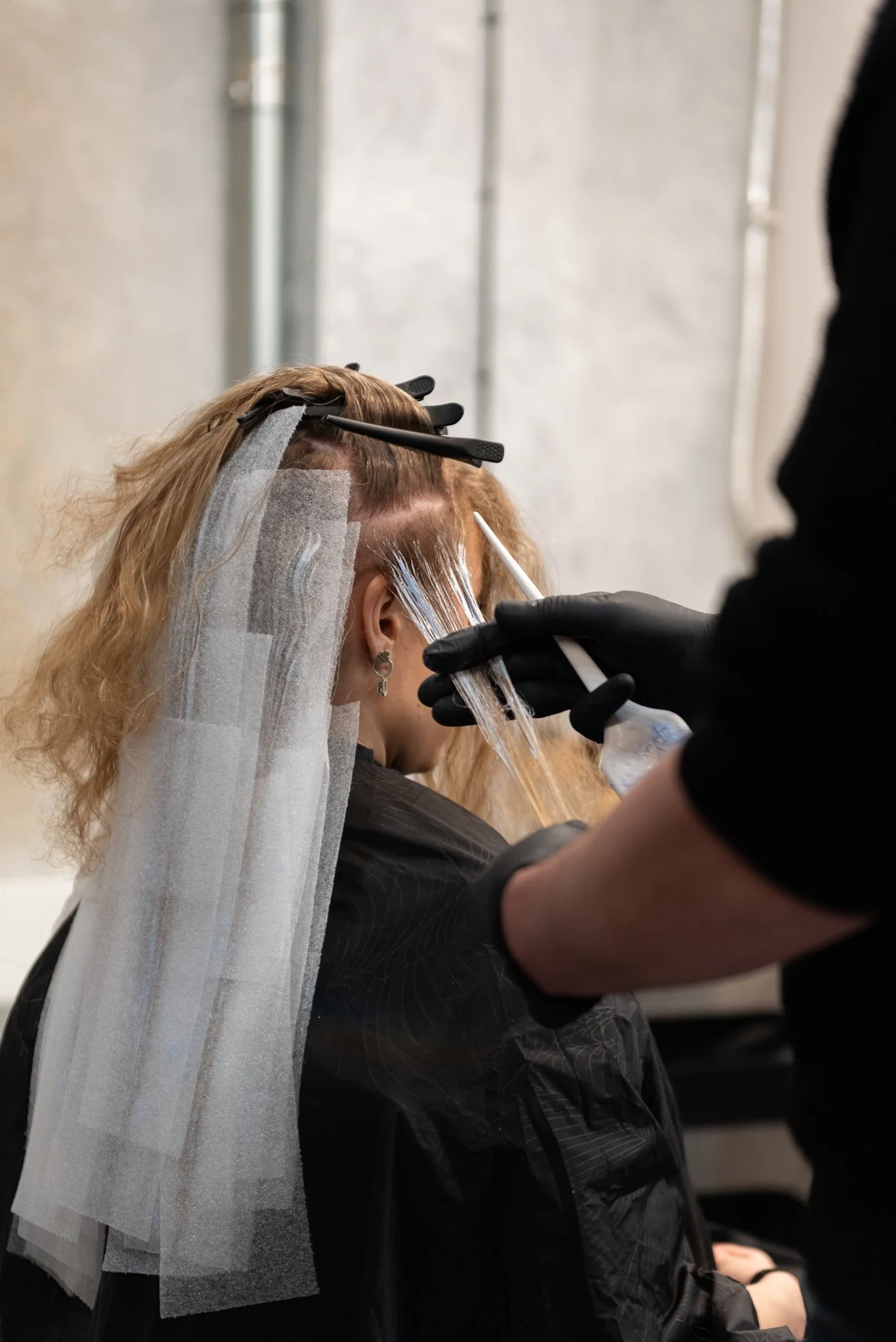 A person getting their hair dyed by a professional in a salon, with protective sheets and gloves.