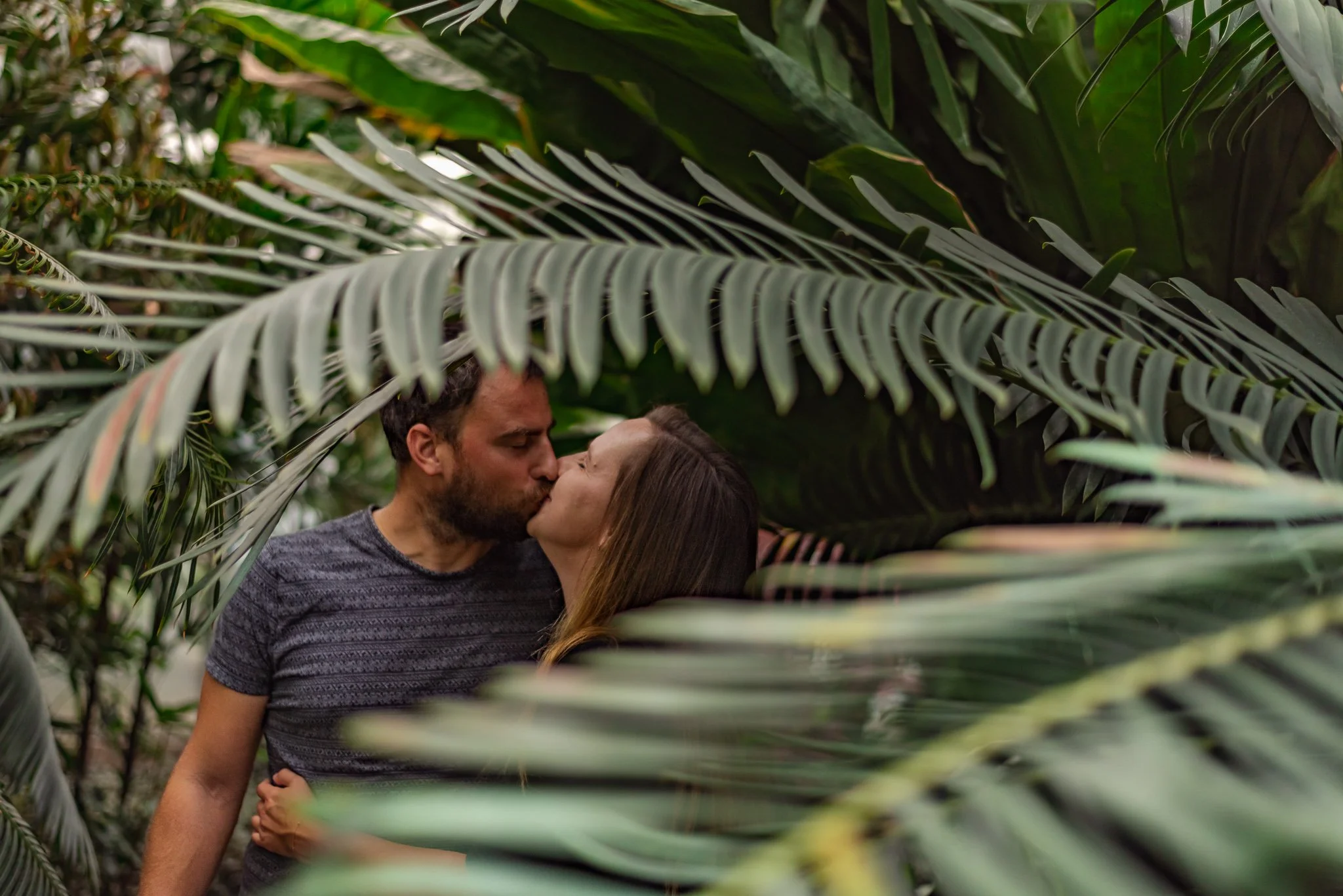 A couple sharing a kiss among lush green tropical plants.
