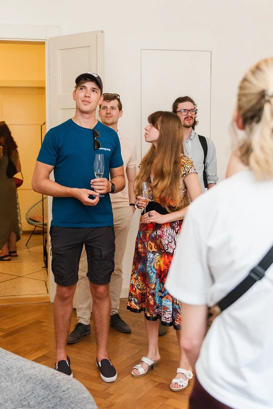 Group of young adults at a social gathering, some holding wine glasses, standing and talking indoors. Event photography in Prague.