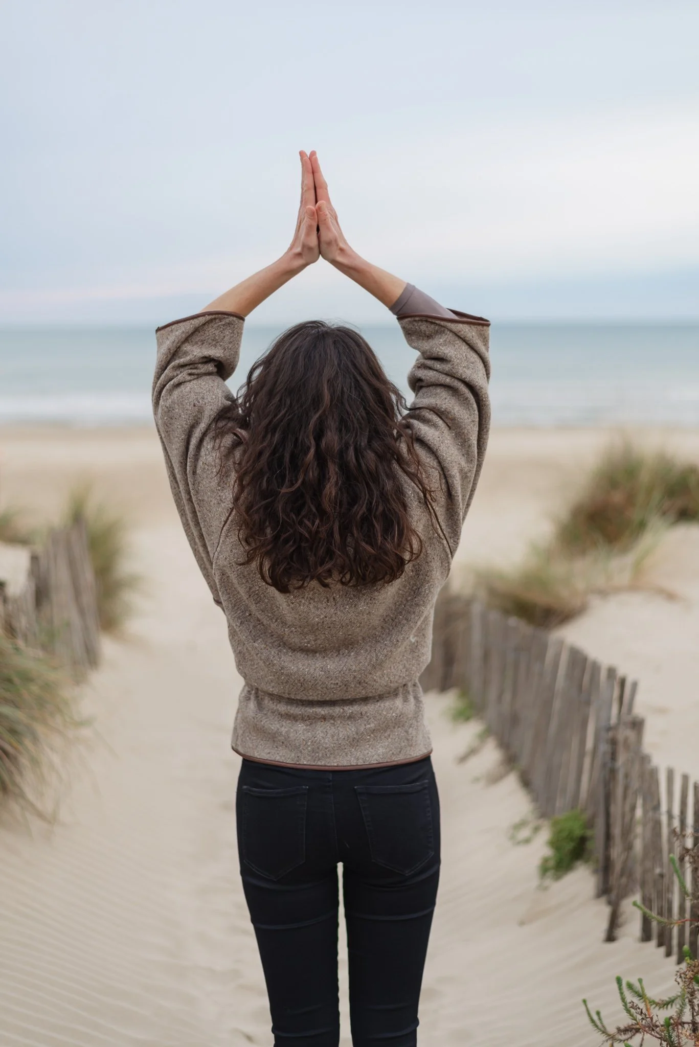 lifestyle picture of a girl from the back at the beach joining her hands together towards the sky