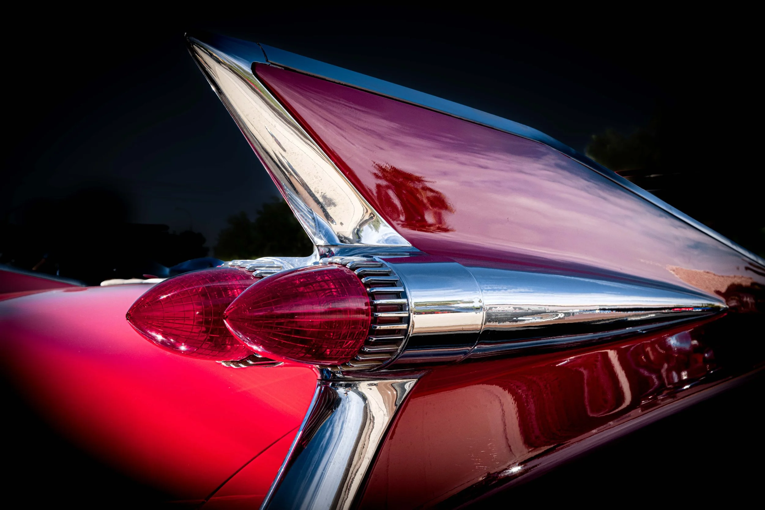 Close-up of a classic red car's tail fin and tail lights with chrome accents, featuring a mid-20th-century retro design.