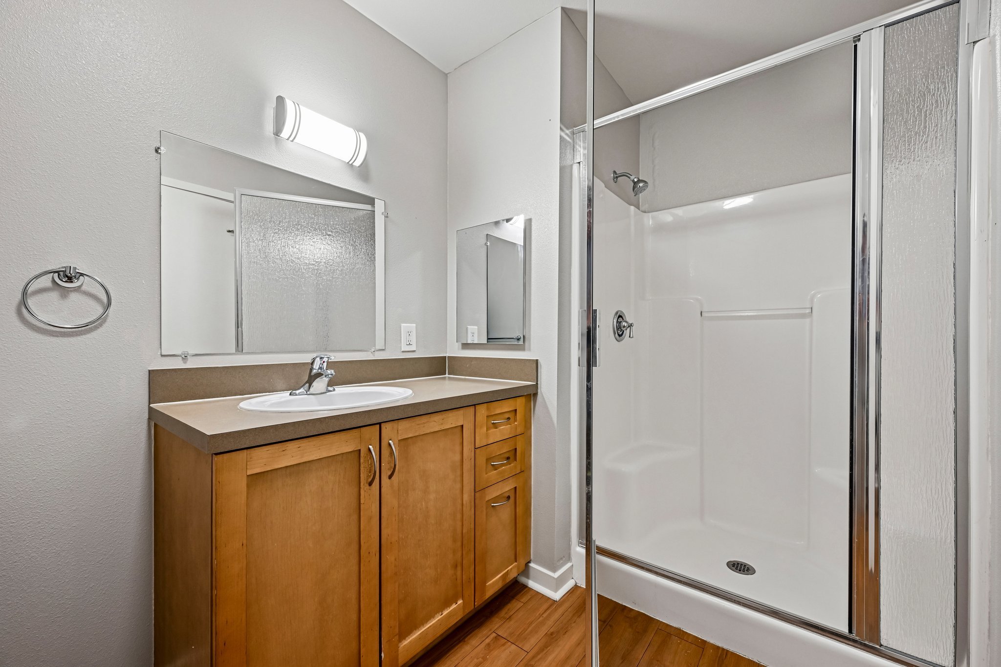 Bathroom with a wooden vanity, a sink, a large mirror, a towel ring, and a shower with a sliding glass door.