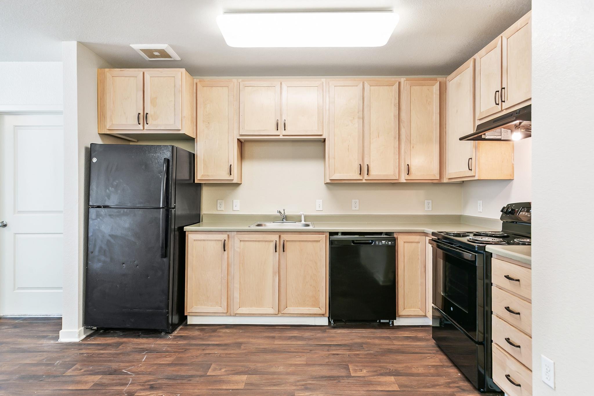 Kitchen with upper and lower cabinets, a black refrigerator, a black dishwasher, a stove, a sink, and electrical outlets on the wall.