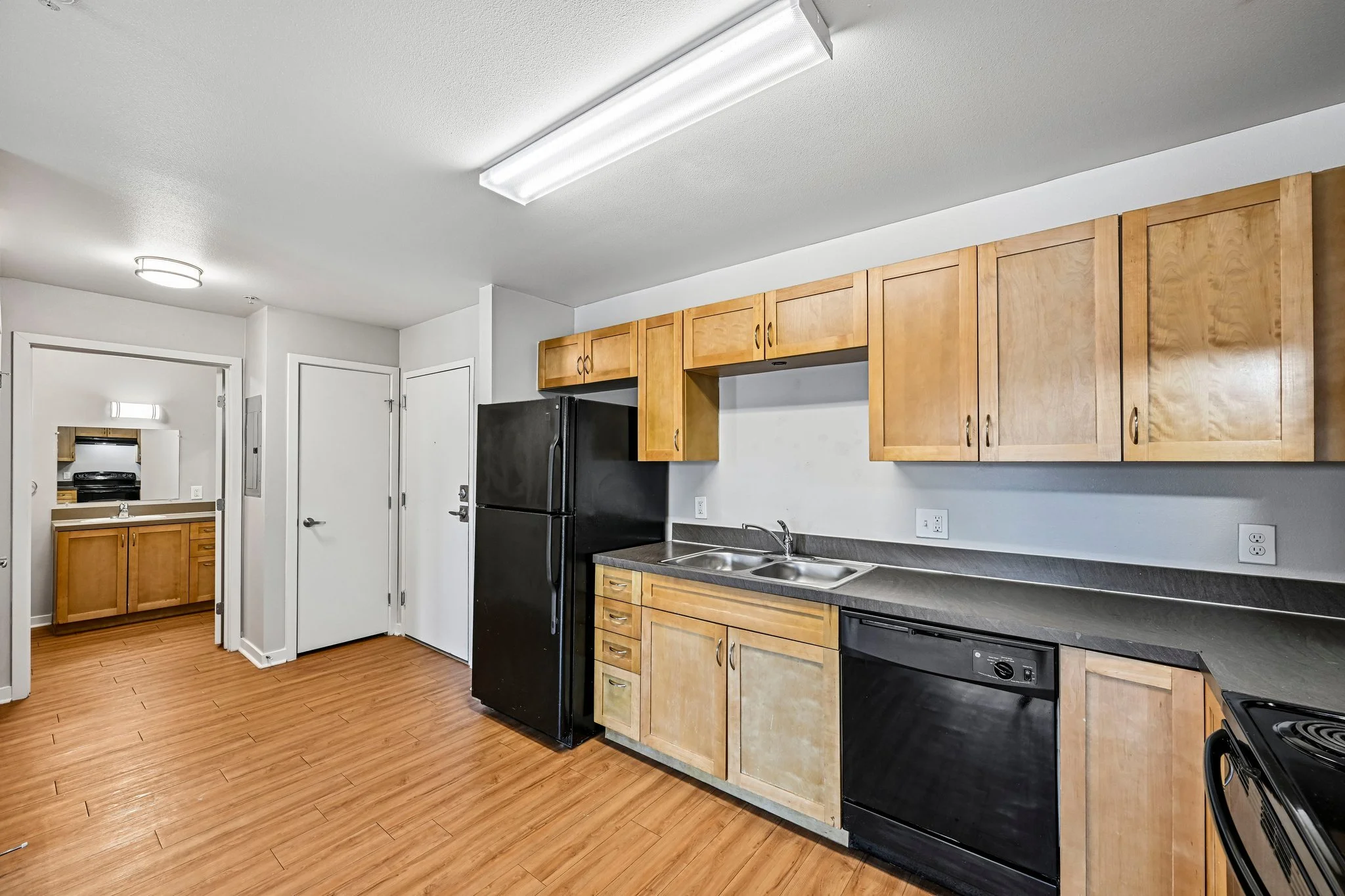 Kitchen with wooden cabinets, black refrigerator, sink, stove, wood-look flooring, and white walls.