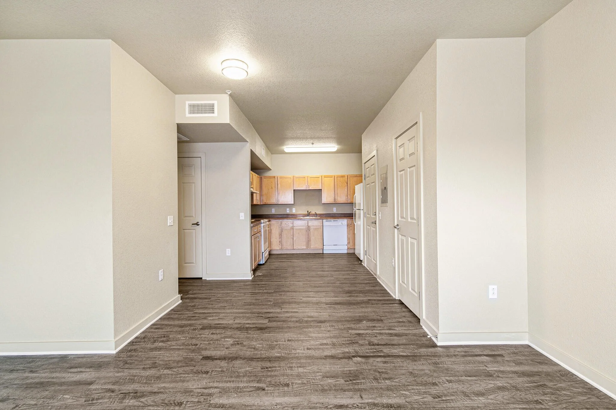 Open-concept kitchen with light wood cabinets, white appliances, beige walls, and wood-look flooring.