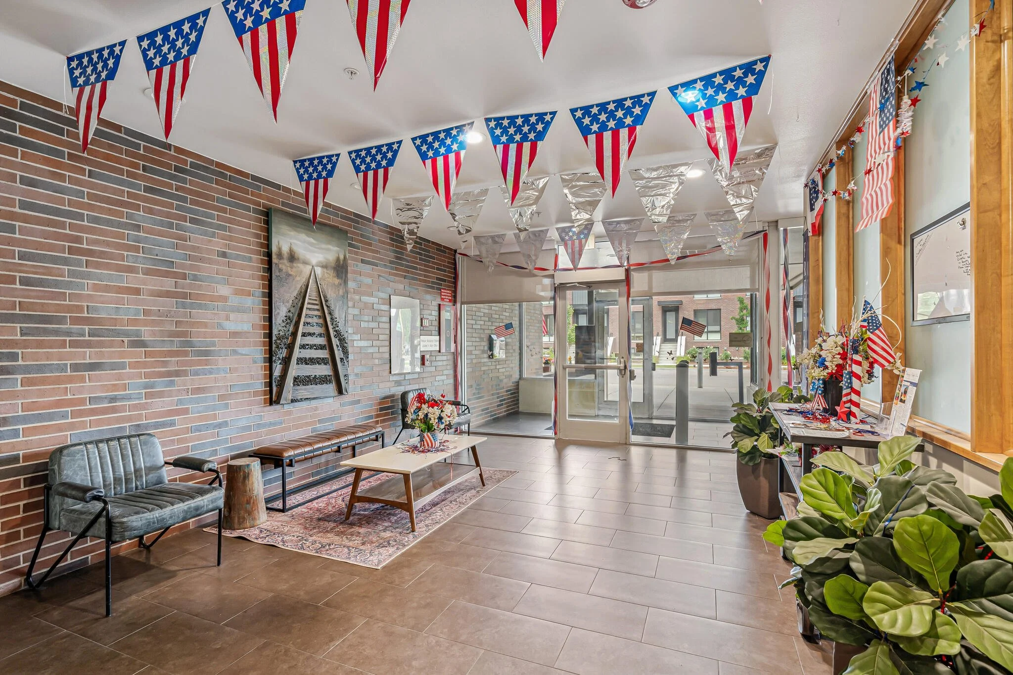 The interior of a building decorated with American flags and patriotic bunting for a celebration, with chairs, tables, and plants.