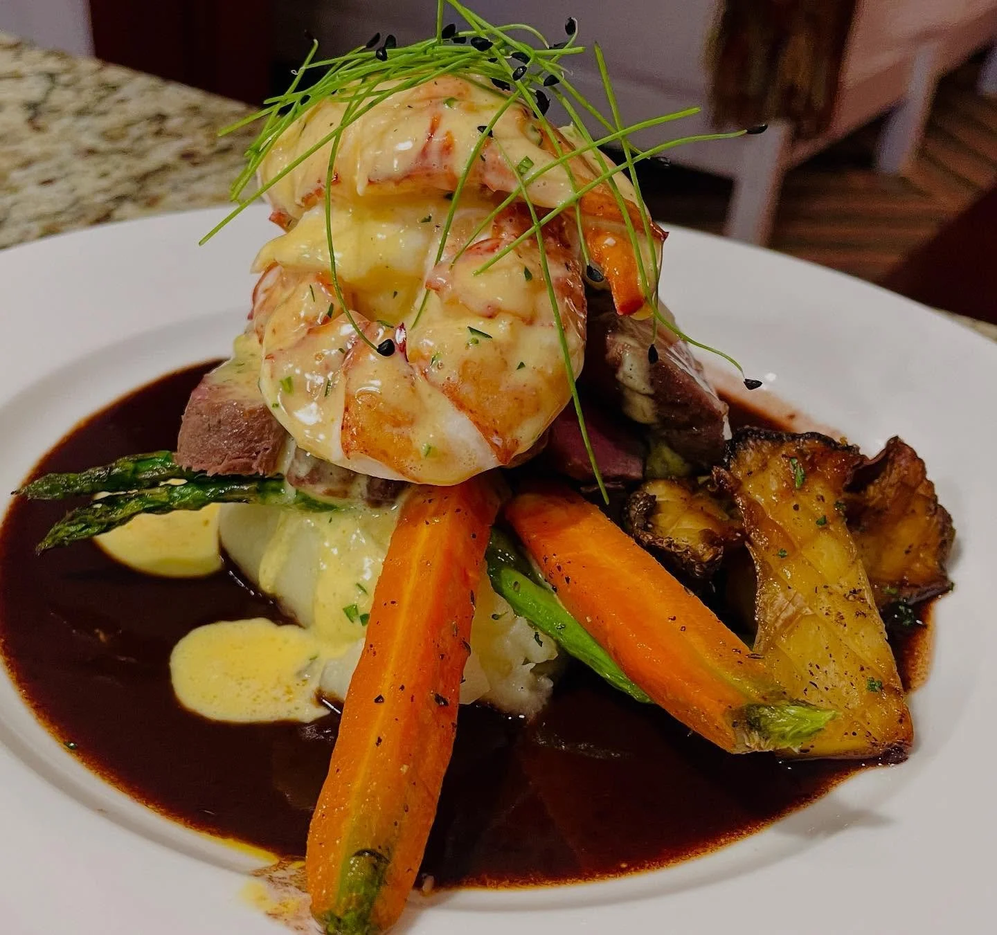 Surf & Turf, elevated. 🌊🔥
Perfectly seared filet mignon topped with butter-poached  Maine  Lobster, garlic mashed potatoes, roasted Maui  heirloom carrots, and asparagus over a red wine demi-glace. Finished with a silky hollandaise and microgre