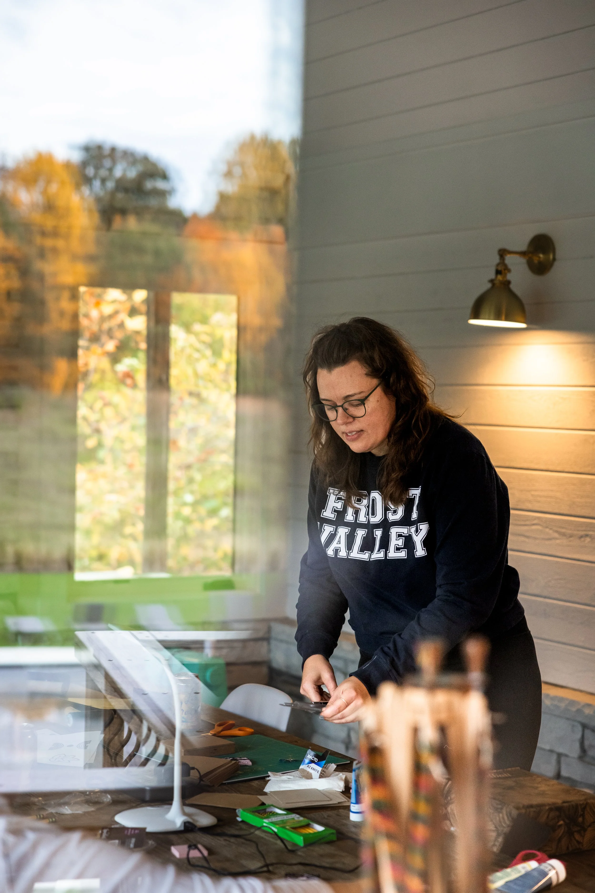 woman in a navy sweatshirt prepares items to teach a knitting class in a beautiful cabin environment