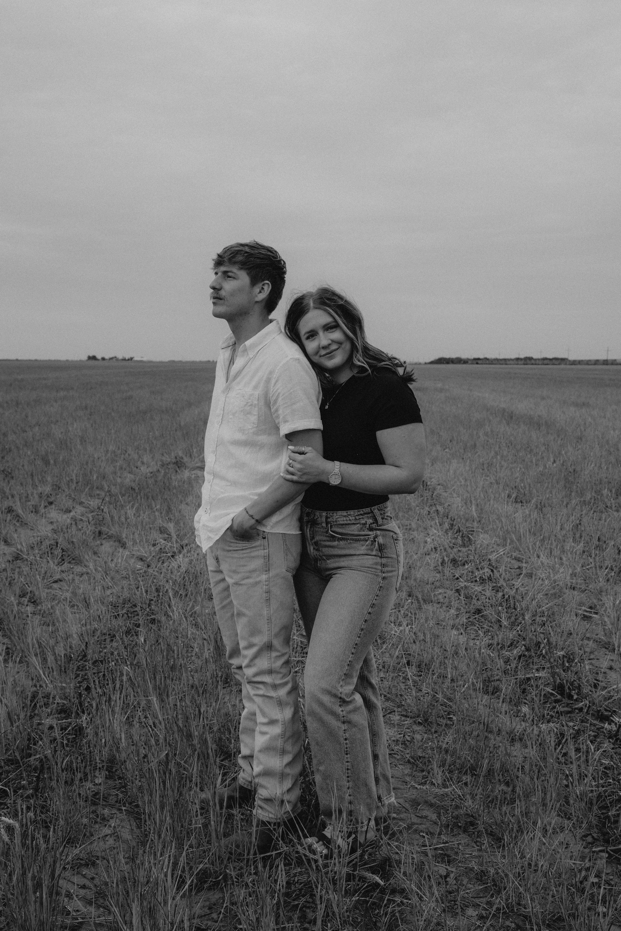 Black and white photo of a couple standing in a grassy field, portrait photography