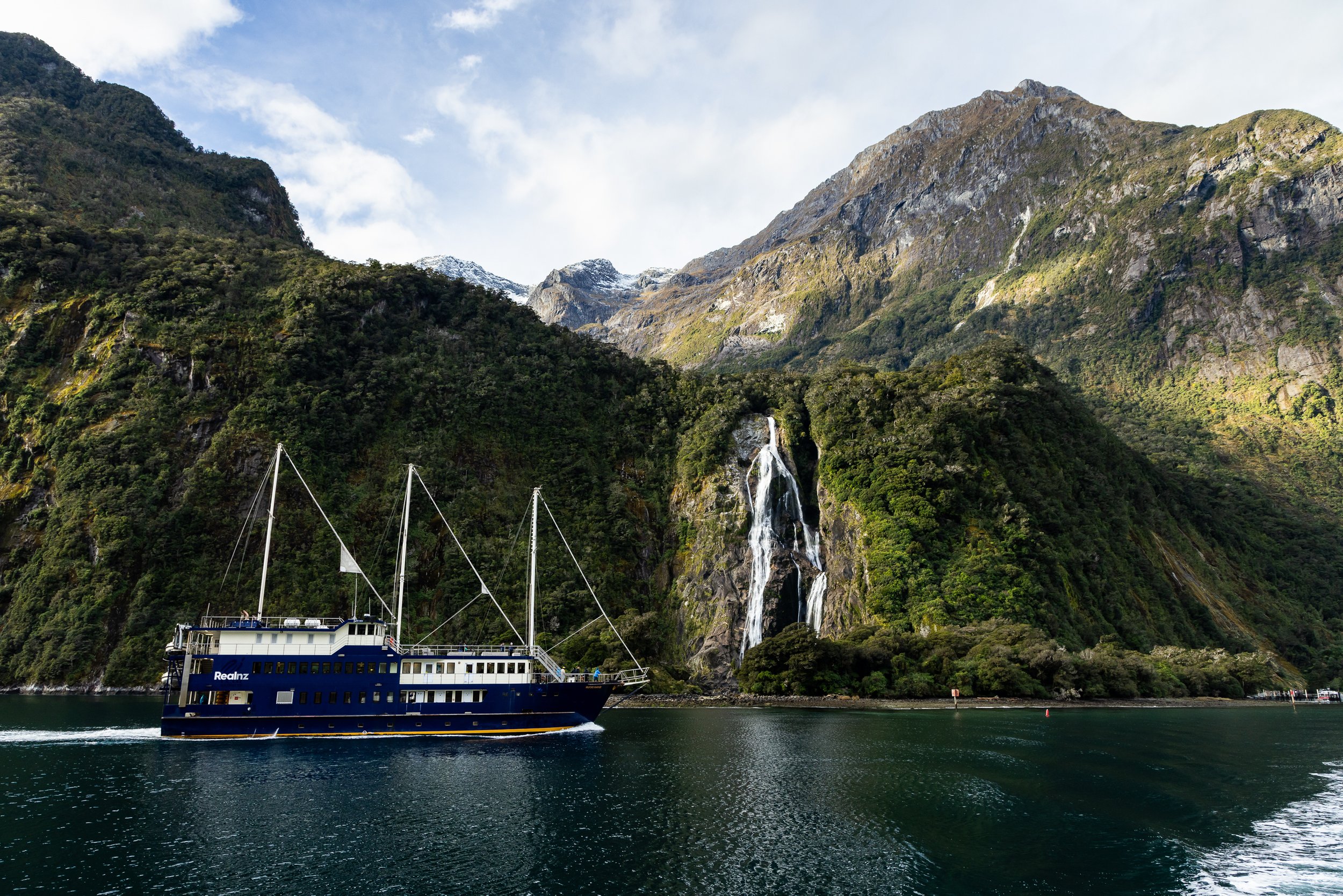 Milford Sound New Zealand landscape with tour boat, waterfall, and dramatic mountain scenery