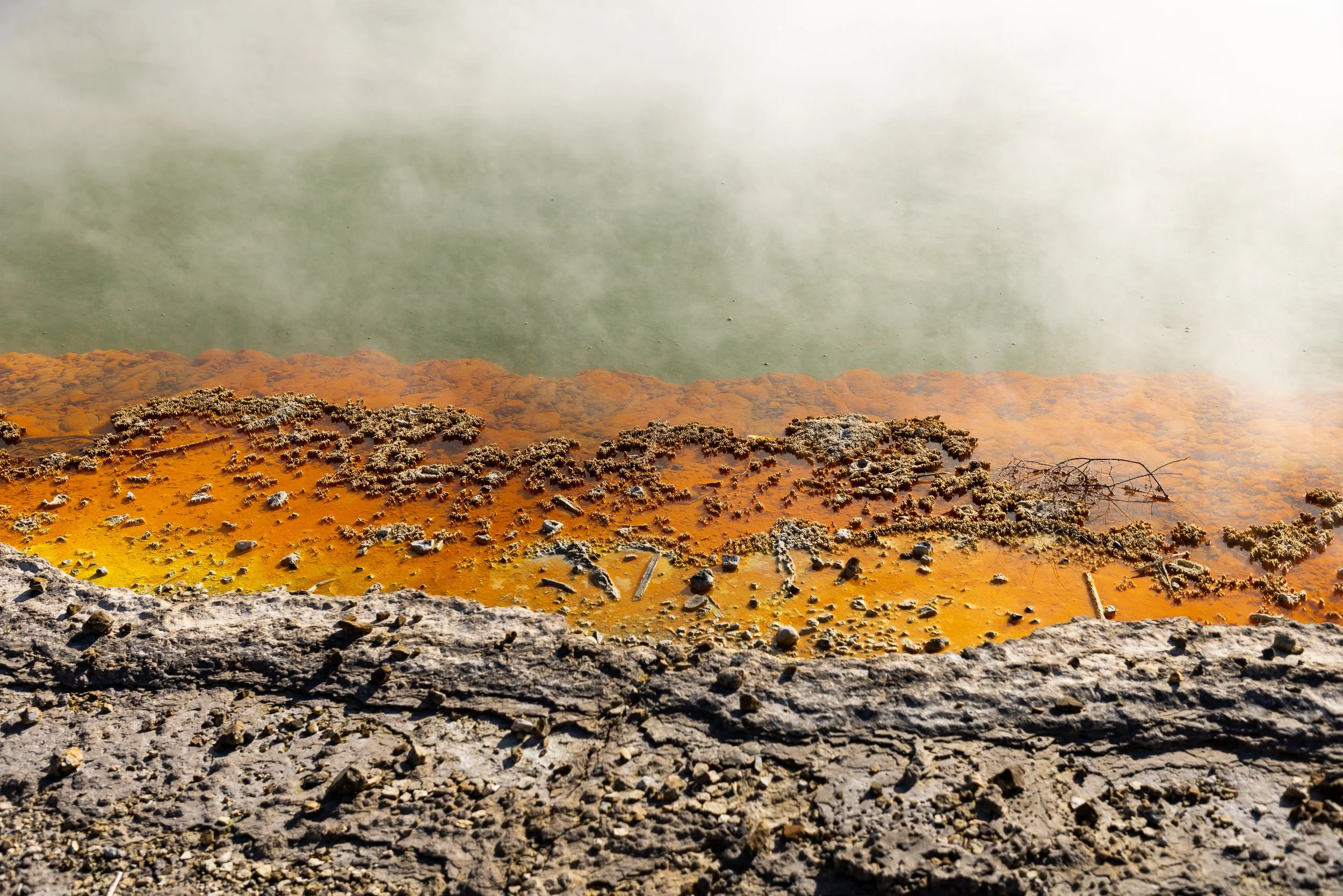 Steaming geothermal pool with bright orange mineral water and textured rocky foreground