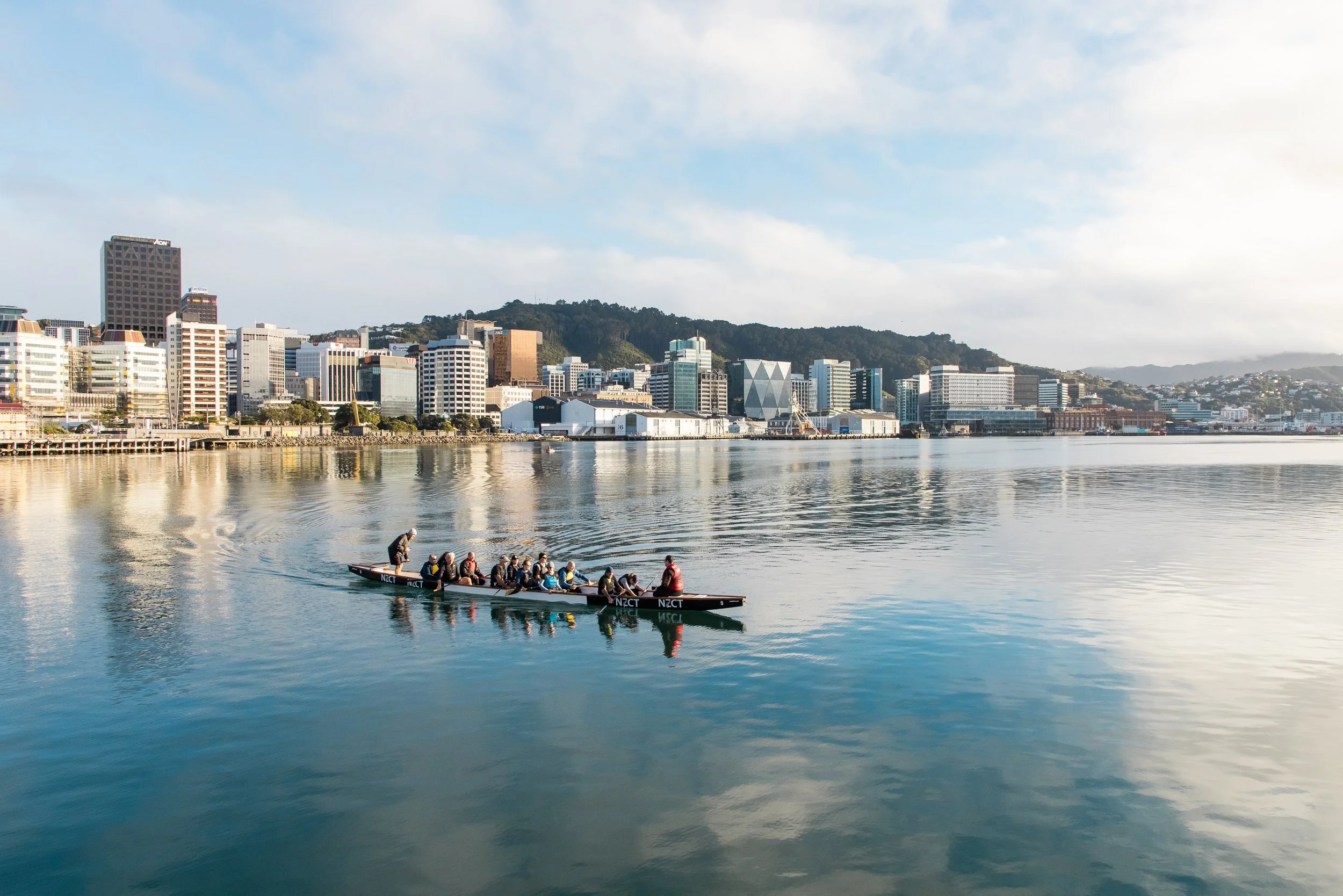 Rowers on calm water with Wellington New Zealand skyline and reflections in the harbor