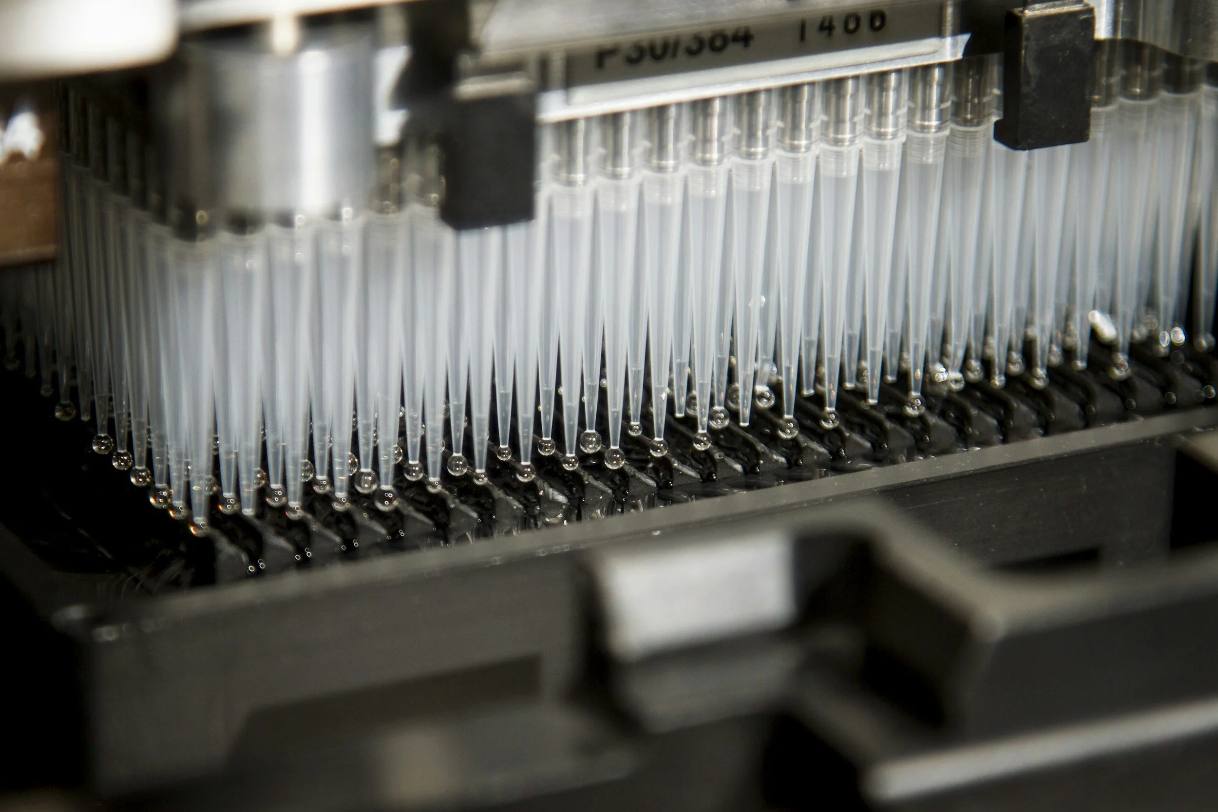 Close-up of a laboratory pipetting machine with multiple pipettes dispensing liquid.