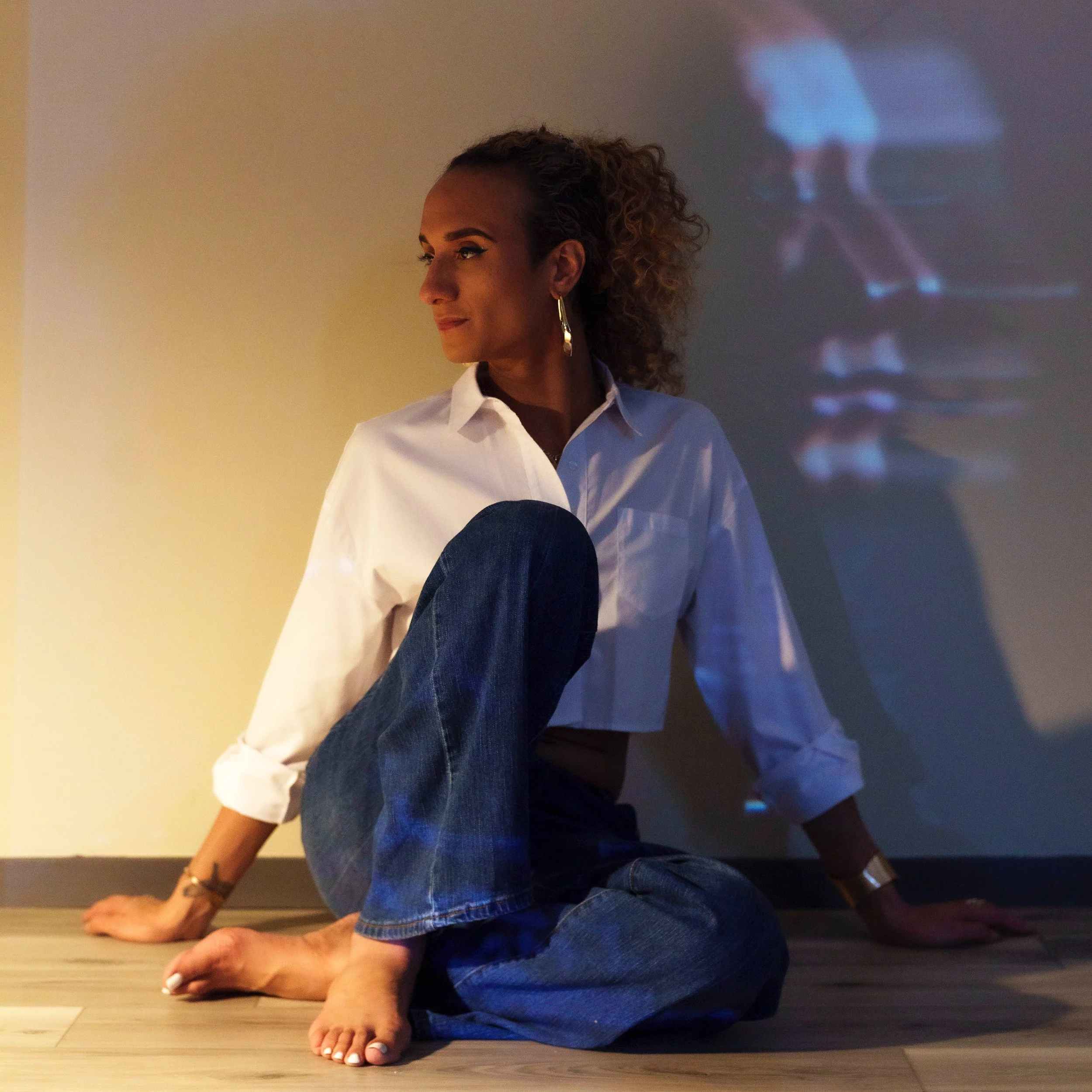 Justy sitting on the floor wearing a white top and blue jeans