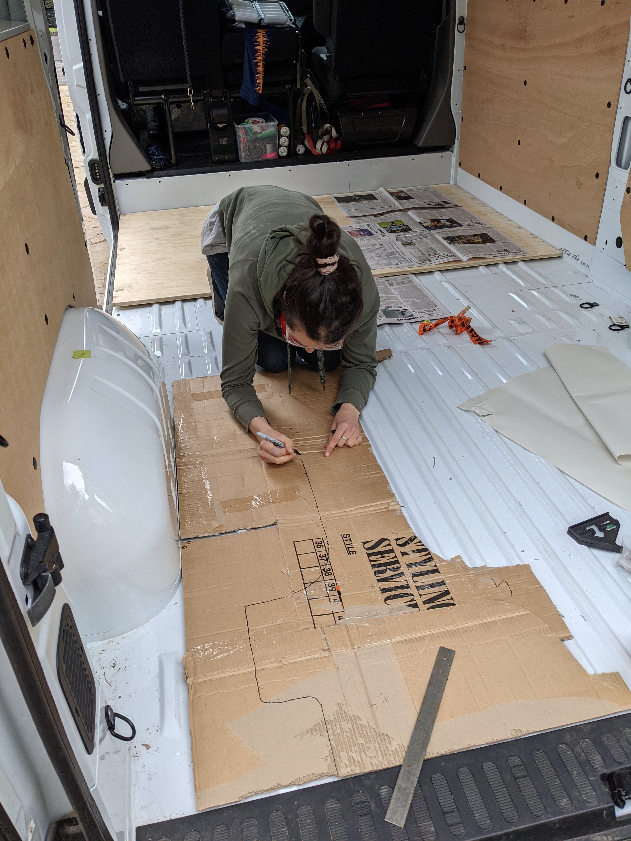 Van builder scribing cardboard subfloor template in van