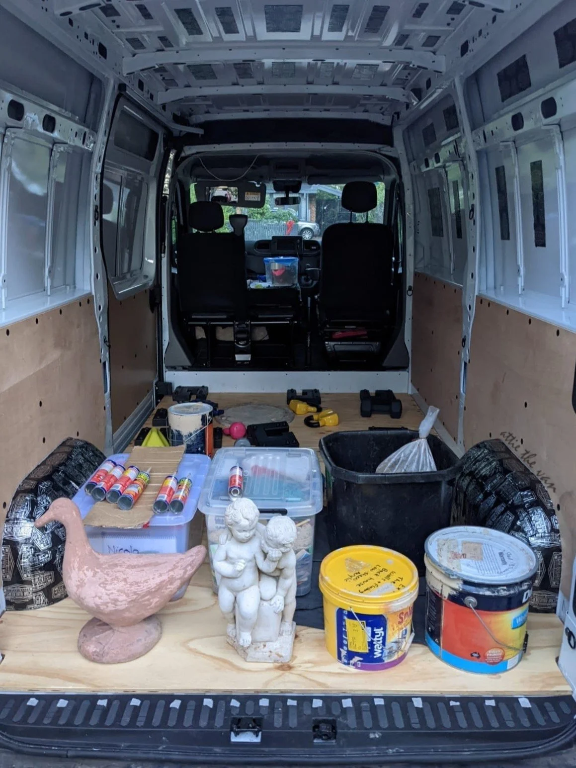 Range of heavy objects (weights, small statues, paint cans) sitting on subfloor in van