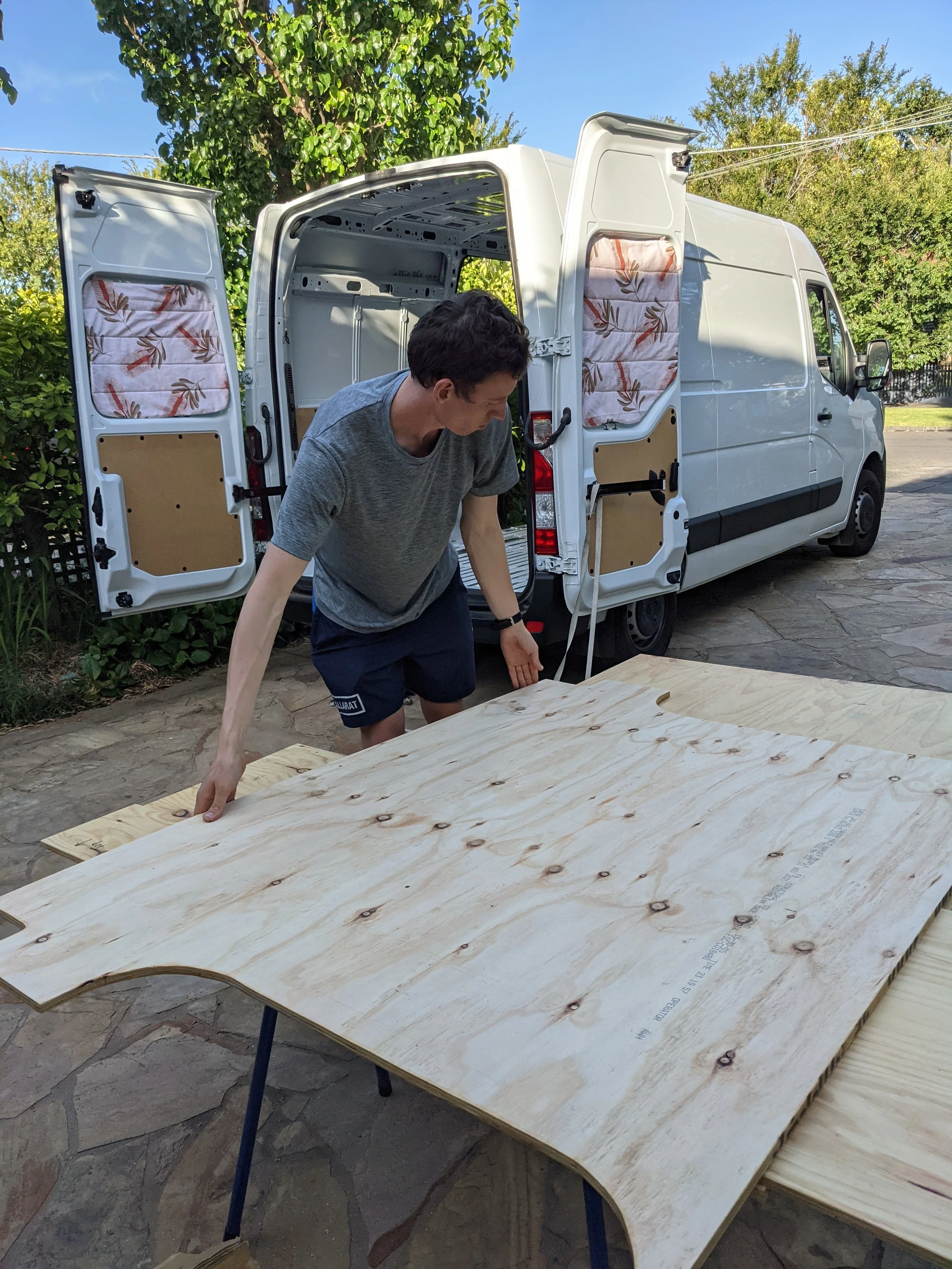 Van builder moving wood subfloor with van in background