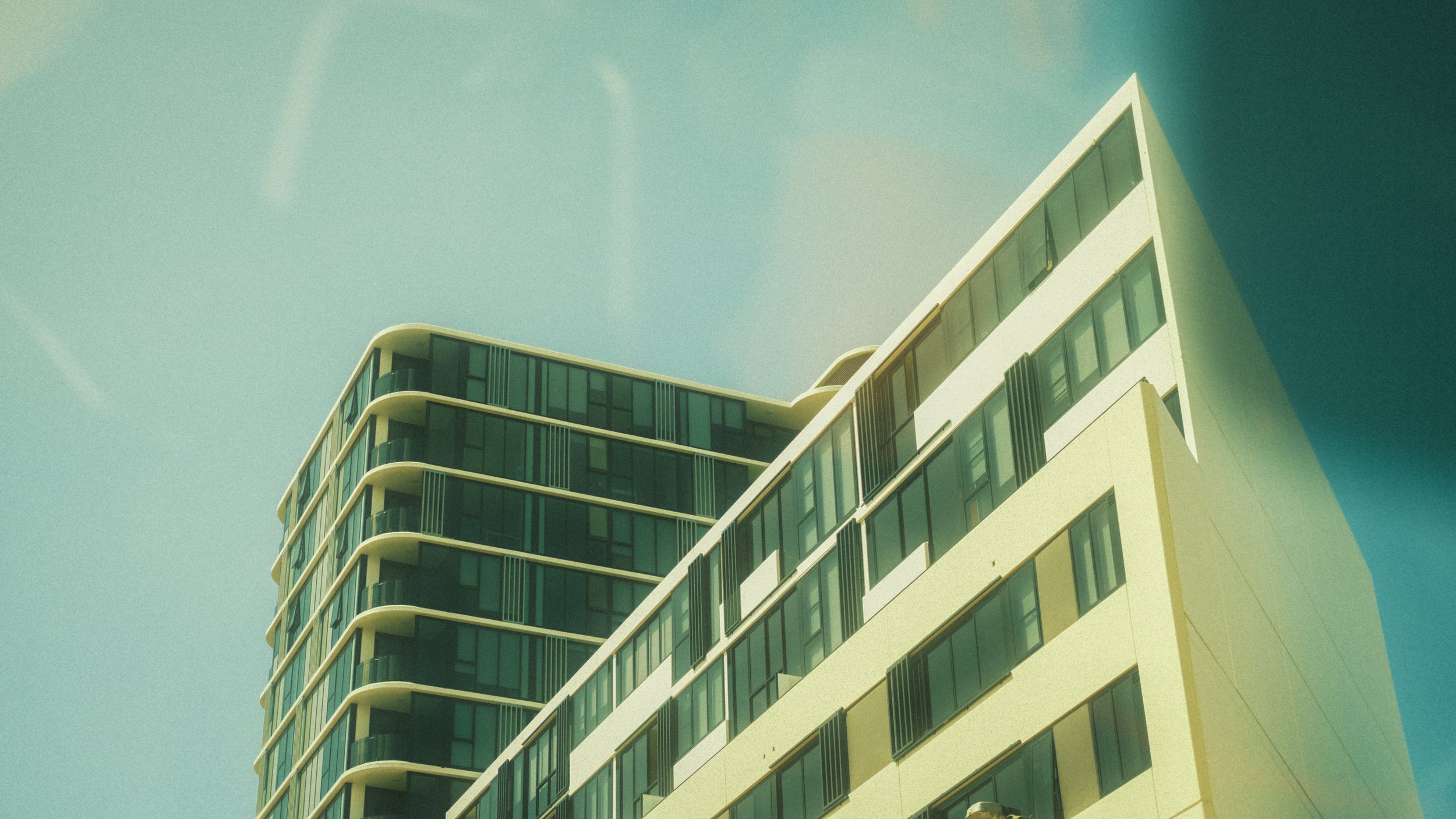 A modern multi-story building with large glass windows and curved balconies, set against a clear blue sky.