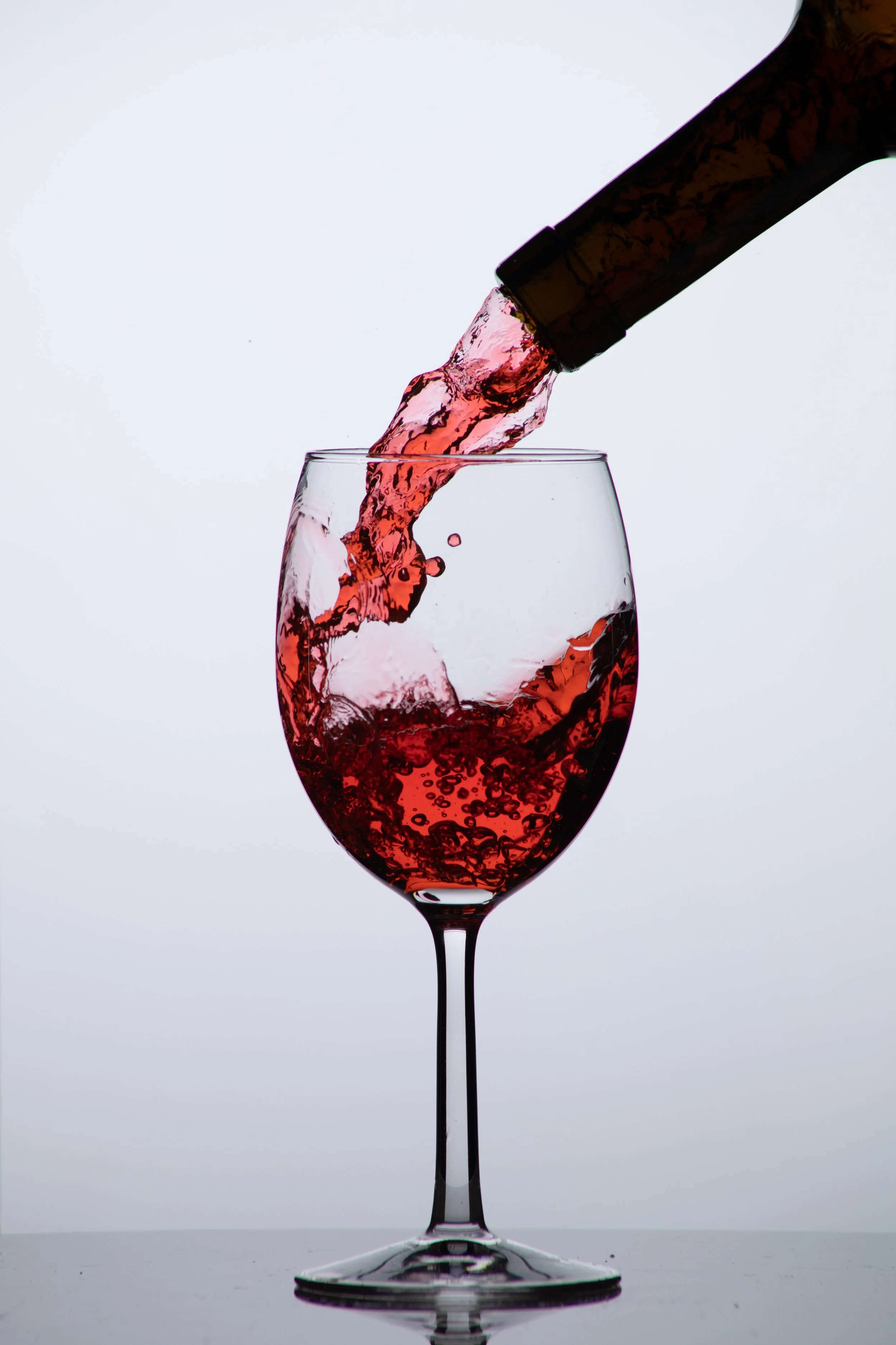 Pink liquid, likely wine, being poured from a bottle into a wine glass against a plain white background.
