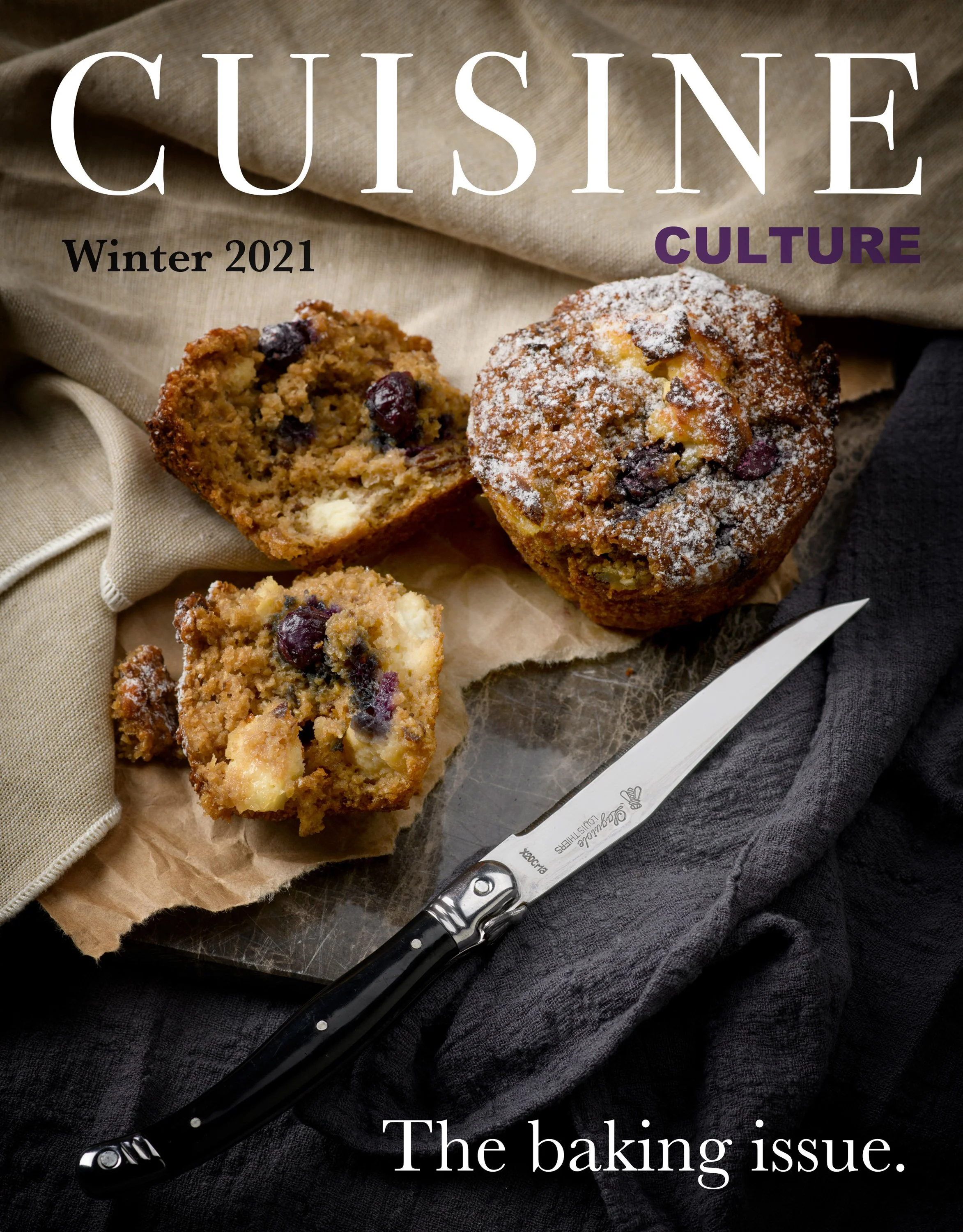 Magazine cover titled "Cuisine Culture Winter 2021" featuring a close-up of blueberry muffins on parchment paper, with one muffin cut open revealing blueberries and white chocolate chips, a black-handled butter knife resting nearby, and a beige cloth