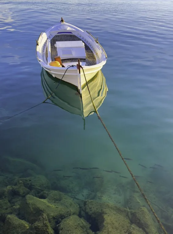 A traditional Greek wooden fishing vessel used for working or fishing, this varka is floating in the calm, early morning water, tied off the pier in Nafplio, Greeece.
