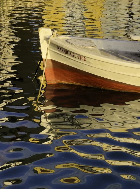 Small ripples create beautiful reflections as a  varka floats in the Venetian Harbor in Nafplio, Greece.