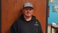 Person wearing a gray cap and dark hoodie standing indoors in front of a wooden door.