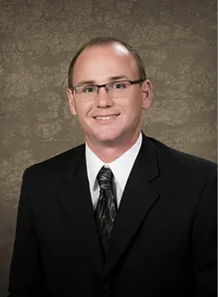 Businessman in a suit with glasses smiling against a textured gray background.