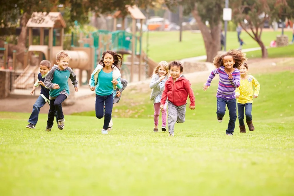 A healthy group of children running towards the camera, smiling and laughing.