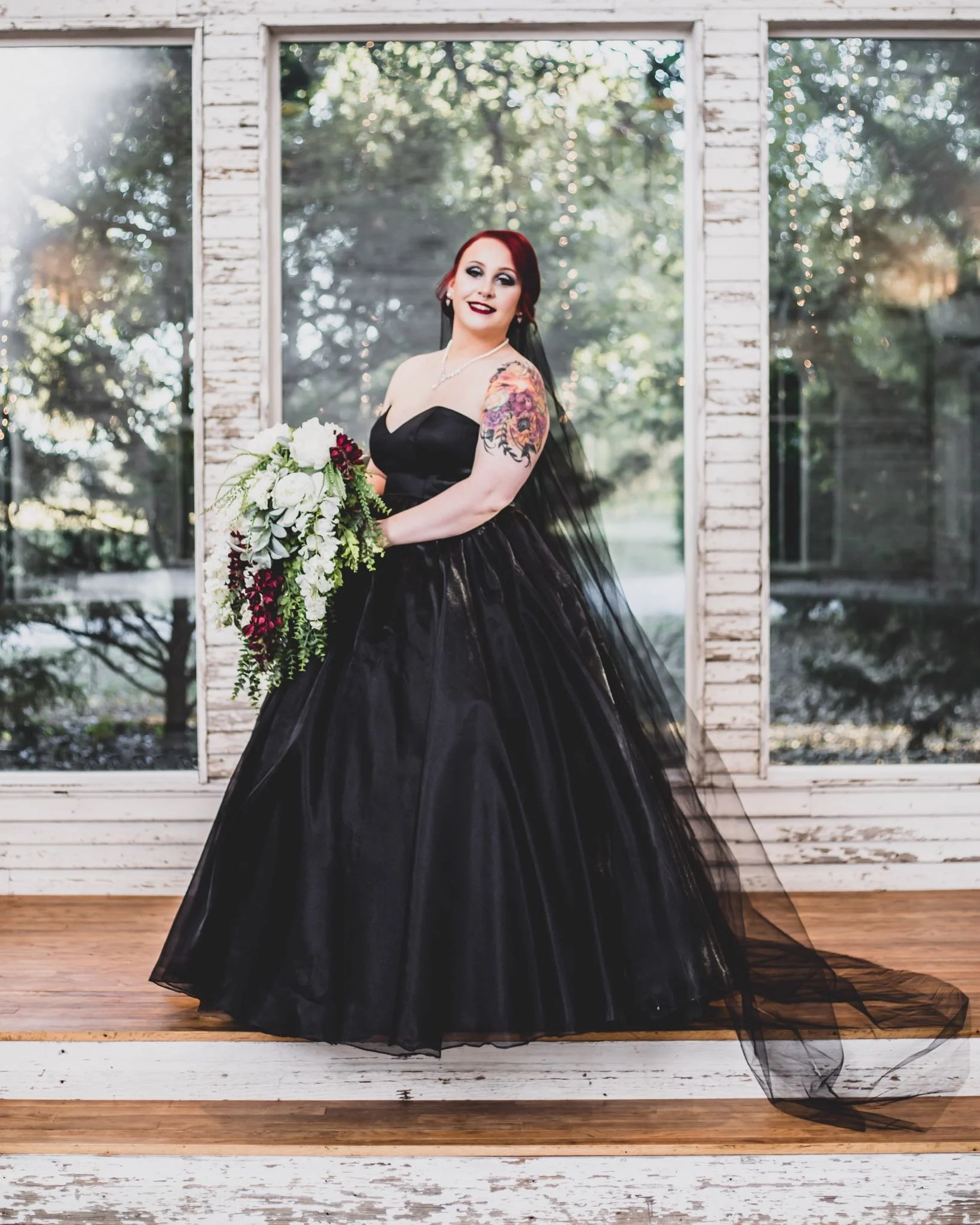 bride with black wedding dress and flower bouquet in front of a window