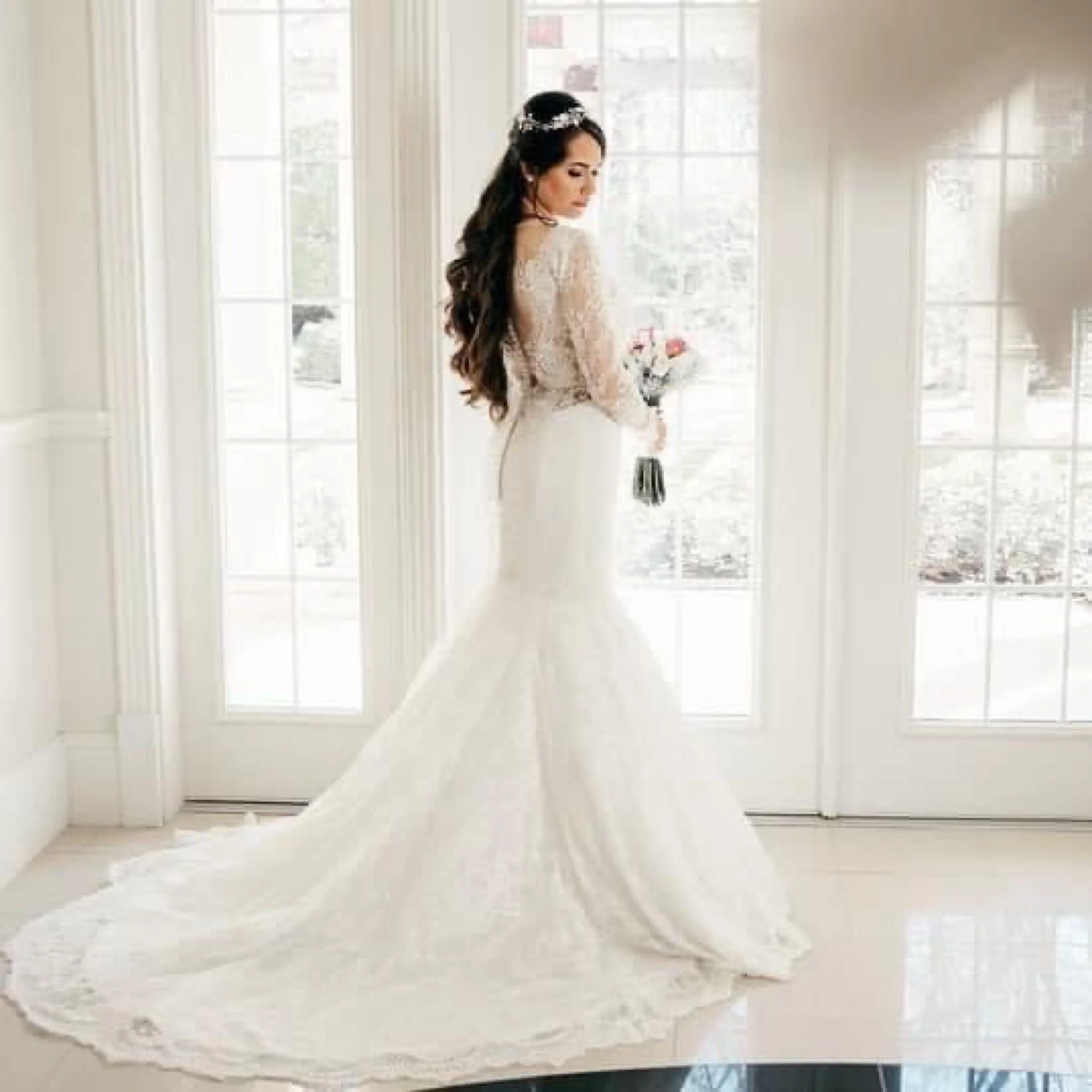 luxury bride posing  in front of a window showing the back of her dress and hair