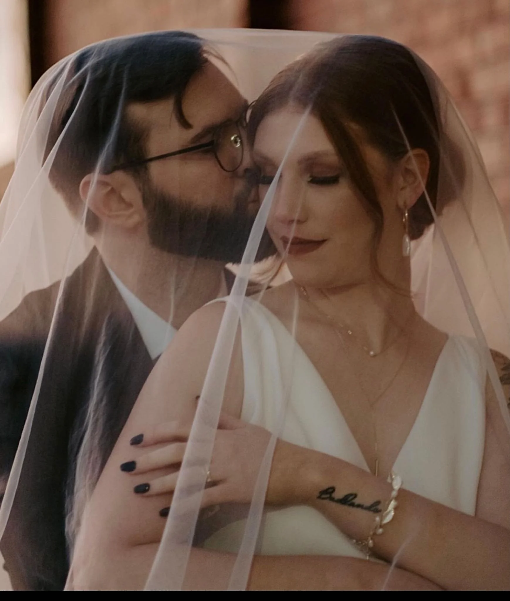 groom kissing bride on the cheek covered by a vail